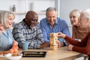 A group of older adults chatting together in a bright, home-like community common area.